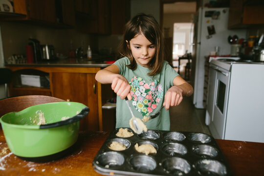A young girl mixes ingredients to bake muffins at home