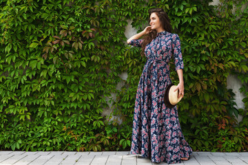 Gorgeous woman wearing beautiful maxi dress posing against wall with a wild grape