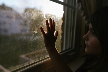 Child's hand touching window as she gazes out window