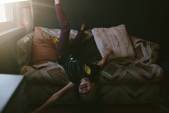 young girl hangs upside down off a couch