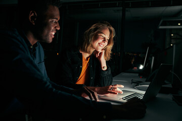 Diverse creative business people working with laptop overtime at night in low light at office