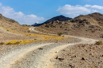 Copper Hike trail, winding gravel dirt road through Wadi Ghargur riverbed and rocky limestone Hajar Mountains in Hatta, United Arab Emirates.