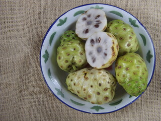 Morinda citrifolia or noni fruit is also known as mengkudu in Indonesia. Popular to used as traditional medicine. Has strong smell and bitter taste. Served on enamel plate. Isolated and copy space.