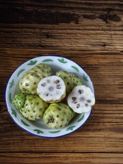 Morinda citrifolia or noni fruit is also known as mengkudu in Indonesia. Popular to used as traditional medicine. Has strong smell and bitter taste. Served on enamel plate. Isolated and copy space.