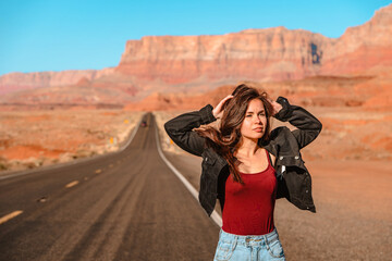 Naklejka premium A beautiful long-haired woman in a denim jacket walks along an empty road in the desert in Arizona with a view of red rocks