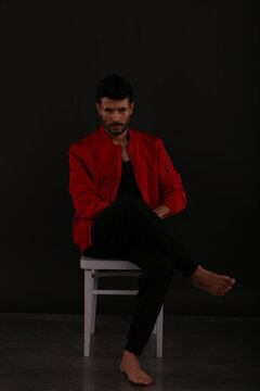 A man in red jacket sitting on a chair on black background