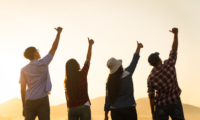 Group of happy friends are having fun with raised arms together in front of mountain and enjoy sunrise sunset showing unity and teamwork. Friendship happiness leisure partnership team concept.