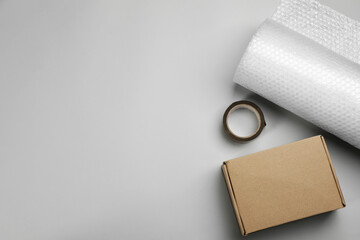 Bubble wrap roll, cardboard box and tape on light background, flat lay. Space for text