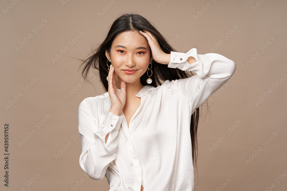 Wall mural beautiful asian woman in a light shirt touches her head and smiles on a beige background