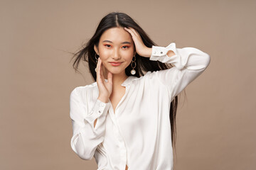beautiful asian woman in a light shirt touches her head and smiles on a beige background
