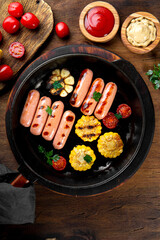  Grilled sausages with vegetables and sauces. Summer BBQ with sausages, corn and tomatoes on the wooden table top view vertical photo