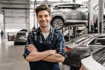 Young white car mechanic smiling while standing in garage indoors