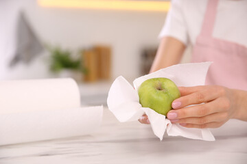 Woman wiping green apple with paper towel in kitchen, closeup