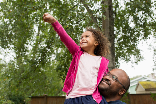 Smilng girl on dad's shoulder raises fist in victory