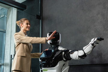cheerful businesswoman gesturing with humanoid robot in office