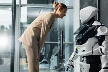 Fototapeta na wymiar smiling businesswoman looking at robot in office