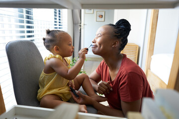 Baby girl having fun painting makeup on mom's face