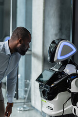 african american businessman looking at robot in office