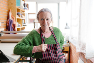 Portrait of elderly grey-haired artisan woman in her workshop smiling at camera.