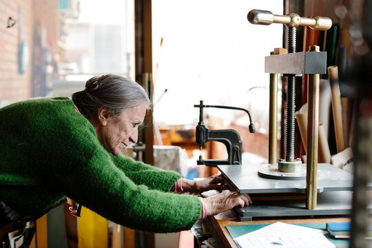 Senior woman adjusting paper in a paper press in a bright workshop
