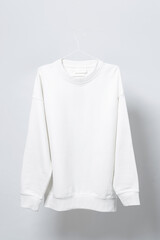 Blank white sweatshirt hanging on a hanger against gray background
