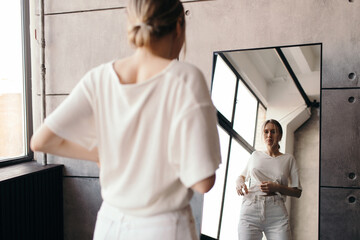 Serious young woman looking in mirror at home
