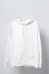 Blank white hoodie hanging on a hanger against gray background