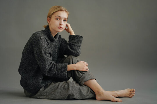 Barefoot young woman in sweater and pants sitting on floor