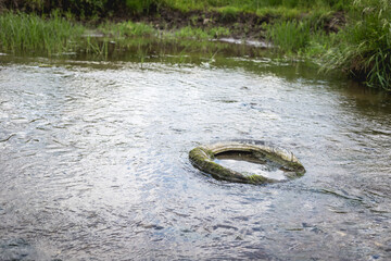 An old car tire in a small river in Ukraine. Environmental pollution concept.