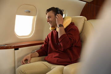 Young man with travel pillow and headphones listening to music in airplane during flight