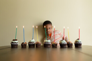 Boy behind row of cupcakes with lit candles