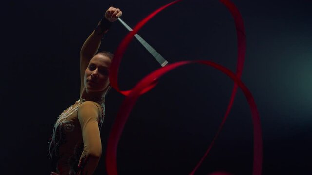 Rhythmic gymnast exercising with ribbon indoors. Girl posing with flying tape.