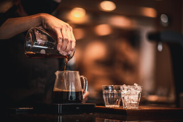 People pouring coffee into jar after drip coffee process at the café. There are water glasses and ice glasses to taste.