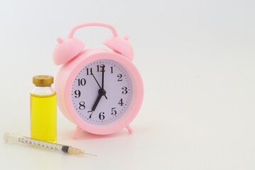 Vaccine bottle and syringe with alarm clock with space for text. Vaccination time concept.