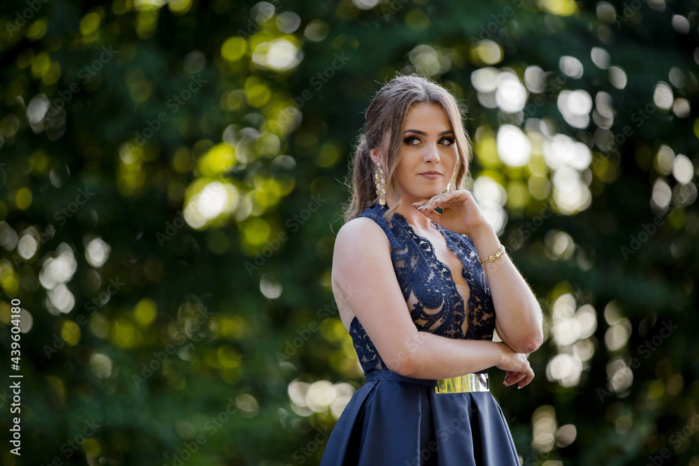 Wall mural Young woman in a blue evening dress posing in the park