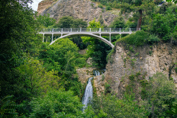Beautiful summer landscape of Botanical Garden – Tbilisi, Georgia – lush foliage, mountains, bridge and waterfall. 
