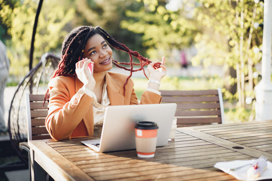 Positive young black woman sitting in outdoor cafe and takling on the phone