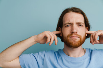 Young ginger man with beard plugging his ears and looking at camera