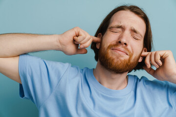 Obraz premium Young ginger man with beard plugging his ears while posing on camera