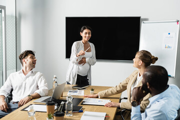pregnant african american businesswoman smiling while talking to multiethnic colleagues