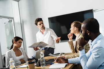 businessman holding newspaper near thoughtful business partners in conference room