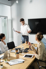 businessman holding newspaper and pointing with hand near interracial business partners