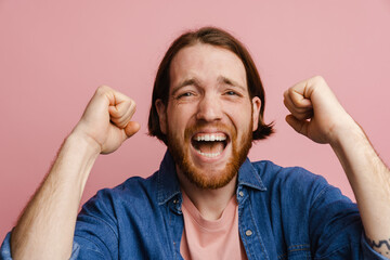 Young ginger man with beard screaming while making winner gesture