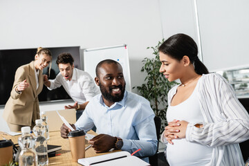 smiling african american business people near document and excited colleagues on blurred background