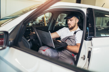 Professional car mechanic working in auto repair service using laptop.