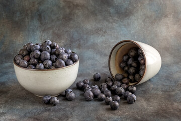Blueberries in a cup, on a wooden table. The berries are scattered on the table. Blurred background. Rustic style. Healthy diet. High quality photo