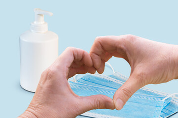 Preventing virus concept with heart shaped hands, protective face mask and soap bottle on blue background. 