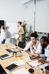 african american businessman pointing at laptop near thoughtful colleague
