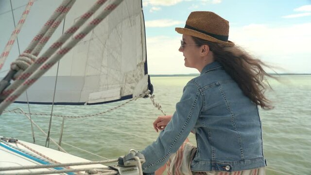 Young woman relaxing on sailing boat enjoying summer vacation. Wind, hat, sunglasses, traveling,