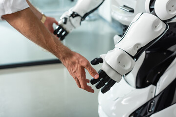 partial view of engineer touching hands of humanoid robot in office